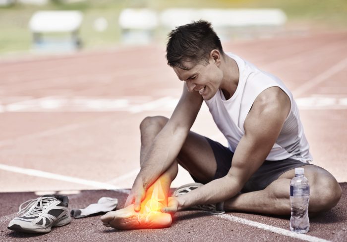 A man sits on a running track holding his ankle in pain.